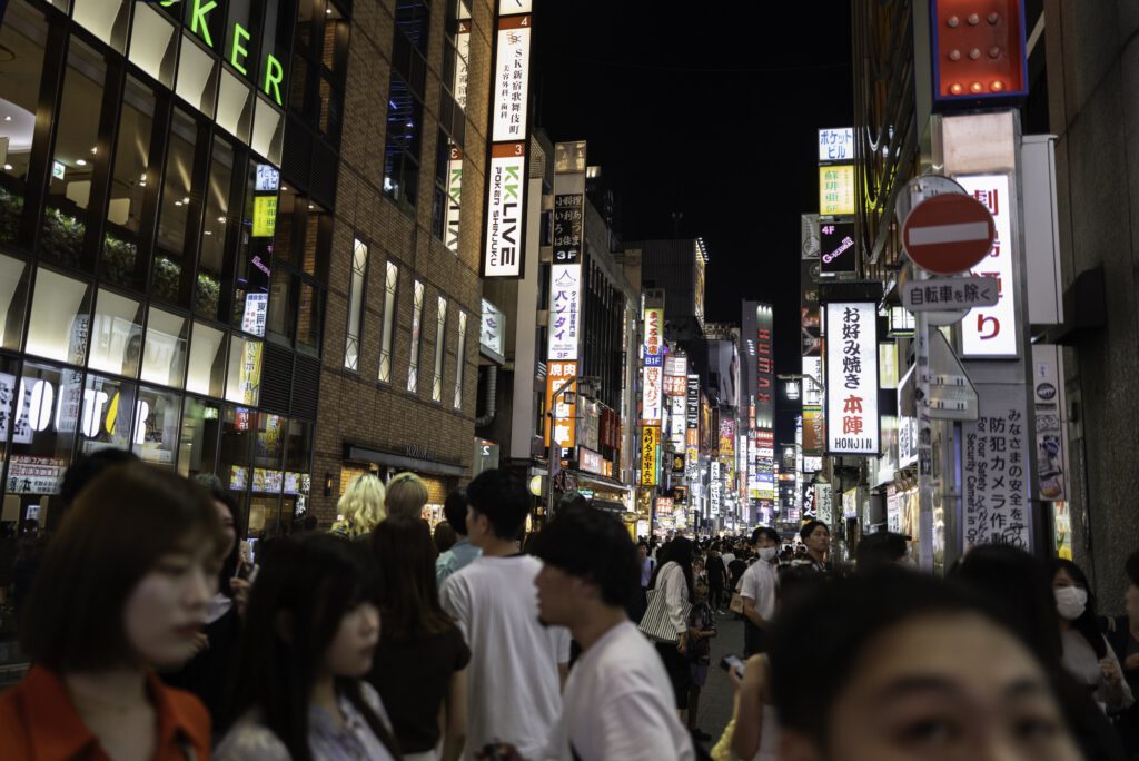 Night view of Kabukicho in Shinjuku, Tokyo, with bright neon signs and a bustling crowd.