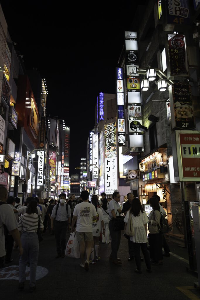 Night view of Kabukicho in Shinjuku, Tokyo, with neon signs and people walking.