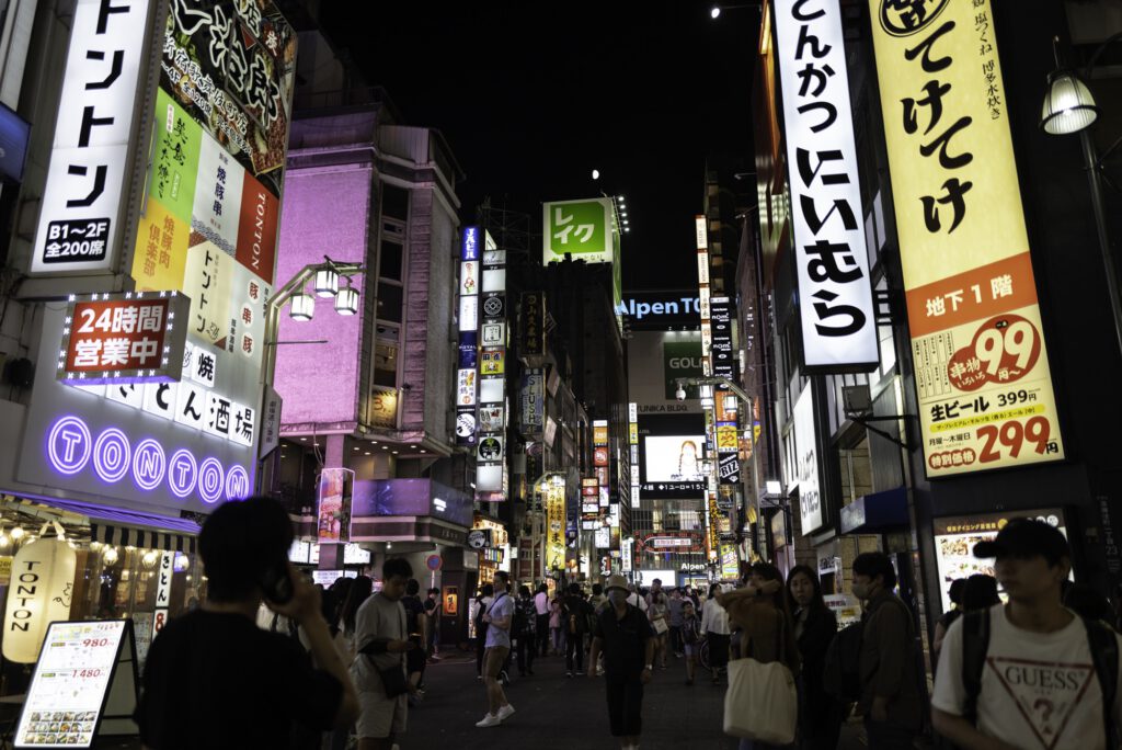 Night view of Kabukicho in Shinjuku, Tokyo, with bright neon signs and people walking.